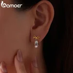 Festliche Weihnachts-Glocken Ohrstecker am Ohr. Detailreiche 925 Silber Ohrringe mit Gold Schleife und Perle. Weihnachtlicher Ohrschmuck.
